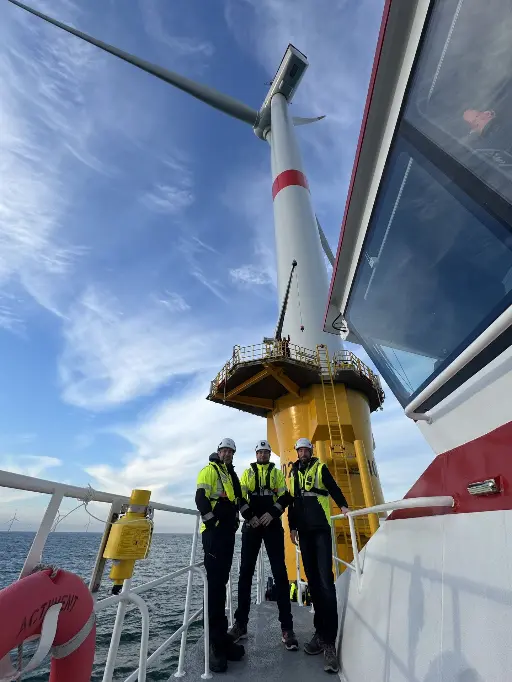 Trois hommes devant une éolienne offshore